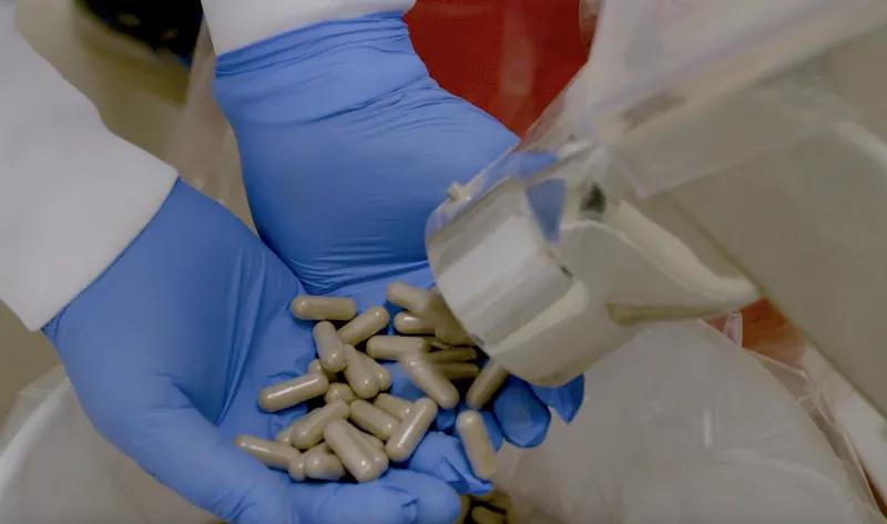 Operator catching finished capsules from the encapsulation line at Adept